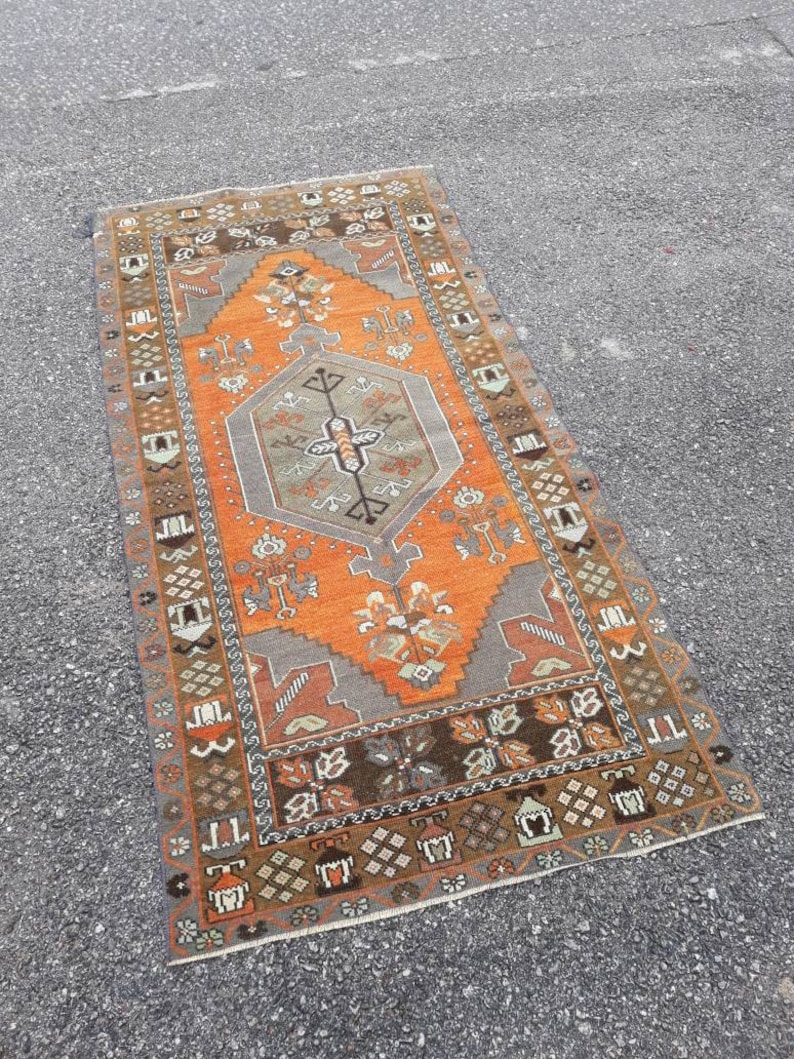 May include: A vintage Turkish rug with a geometric pattern in shades of orange, brown, and gray. The rug has a central medallion and a border with intricate designs.