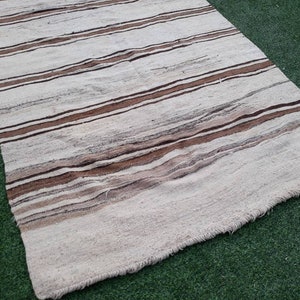 May include: A white and brown striped rug with a fringed edge. The rug is made of a soft, woven material and has a subtle texture.