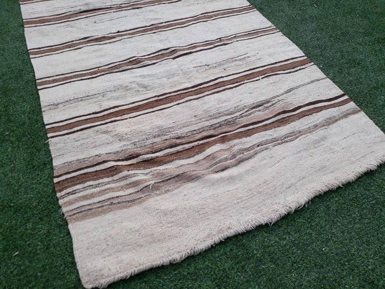 May include: A white and brown striped rug with a fringed edge. The rug is made of a soft, woven material and has a subtle texture.