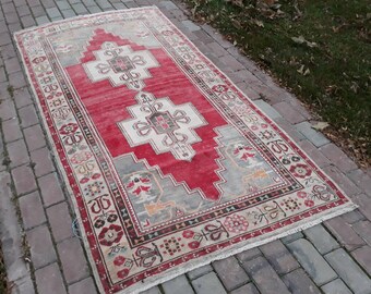 May include: A red and cream colored rug with a geometric pattern. The rug has a fringe border and is made of wool.