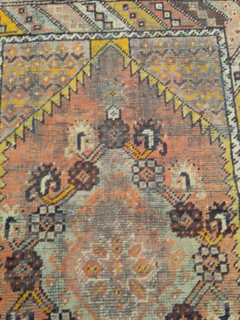 May include: Close-up of a vintage rug with a repeating pattern of geometric shapes and floral motifs in shades of brown, orange, and beige.