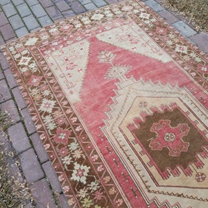 May include: A vintage Turkish rug with a red, brown, and cream color scheme. The rug has a geometric pattern with a central medallion. The rug is in good condition with some wear and tear.