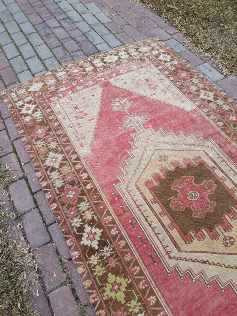 May include: A vintage Turkish rug with a red, brown, and cream color scheme. The rug has a geometric pattern with a central medallion. The rug is in good condition with some wear and tear.
