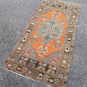 May include: A vintage Turkish rug with a geometric pattern in shades of orange, brown, and gray. The rug has a central medallion and a border with intricate details.