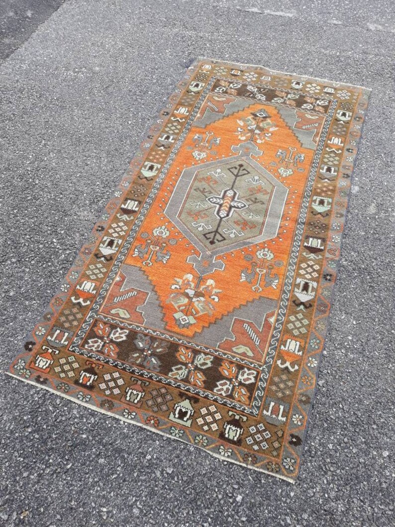 May include: A vintage Turkish rug with a geometric pattern in shades of orange, brown, and gray. The rug has a central medallion and a border with intricate details.