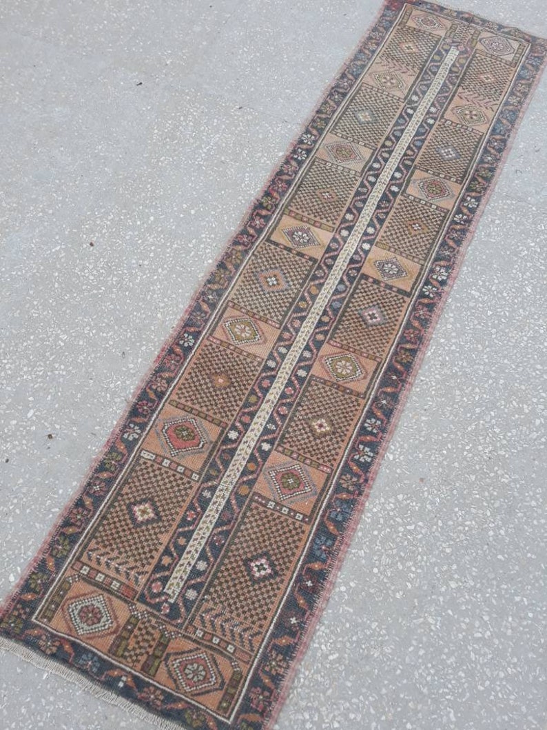 May include: A long, narrow rug with a traditional Persian design. The rug is woven with a variety of colors, including red, brown, and cream. The rug has a fringe on both ends.