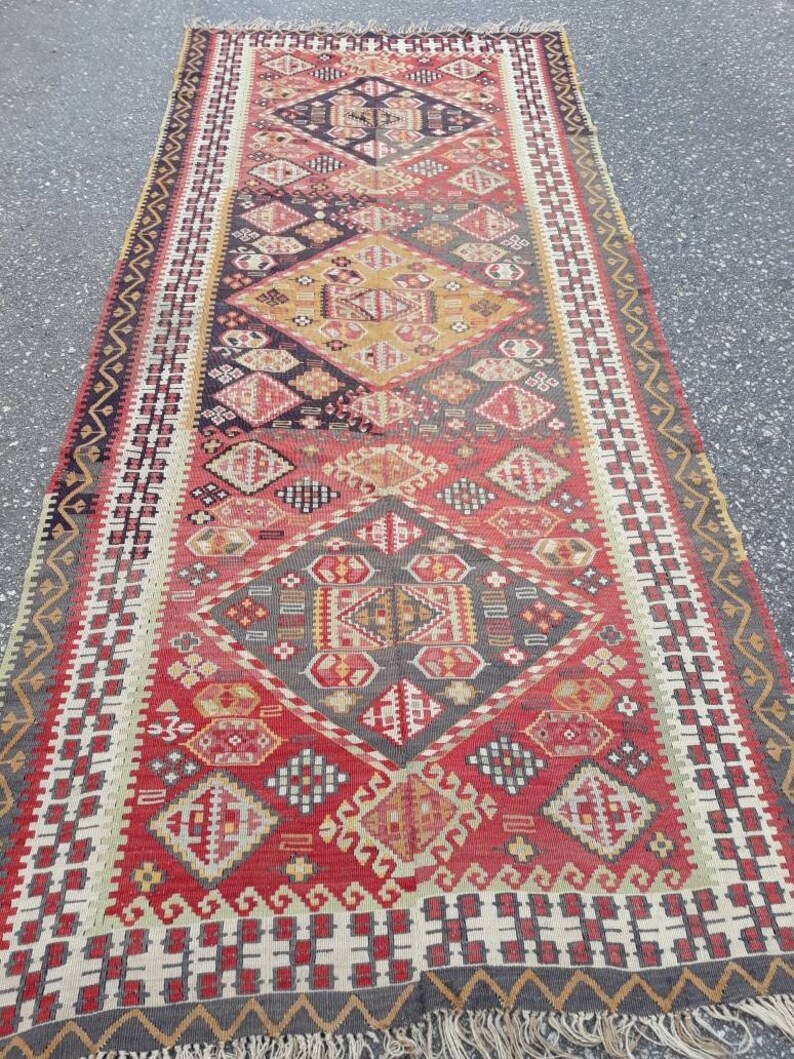 May include: A vintage Turkish rug with a geometric pattern in shades of red, yellow, black, and white. The rug has a fringe border and is woven with intricate details.