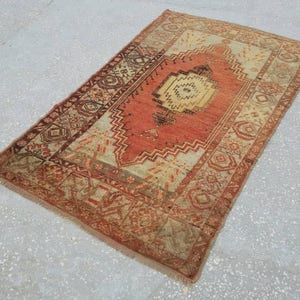 May include: A vintage Turkish rug with a red, orange, and cream color scheme. The rug has a geometric pattern with a central medallion.