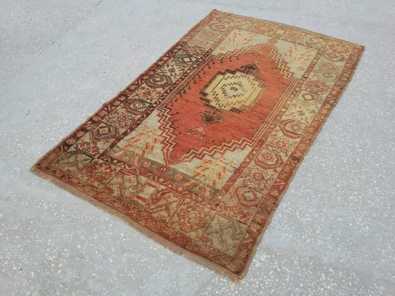 May include: A vintage Turkish rug with a red, orange, and cream color scheme. The rug has a geometric pattern with a central medallion.