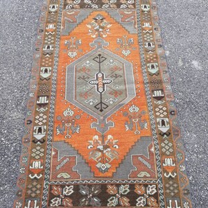 May include: A vintage Turkish rug with a geometric pattern in shades of orange, brown, gray, and white. The rug has a central medallion and a border with intricate designs.