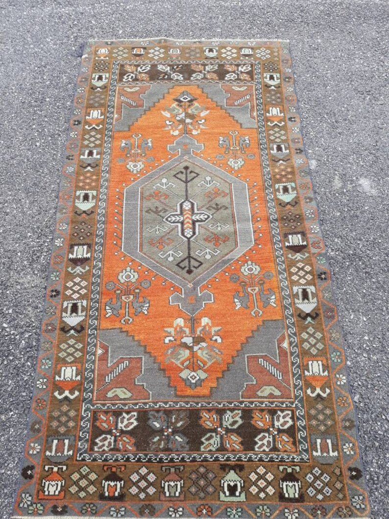May include: A vintage Turkish rug with a geometric pattern in shades of orange, brown, gray, and white. The rug has a central medallion and a border with intricate designs.