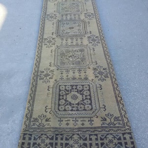 May include: A long, rectangular rug with a beige background and a black and white geometric pattern. The rug has a fringe border.