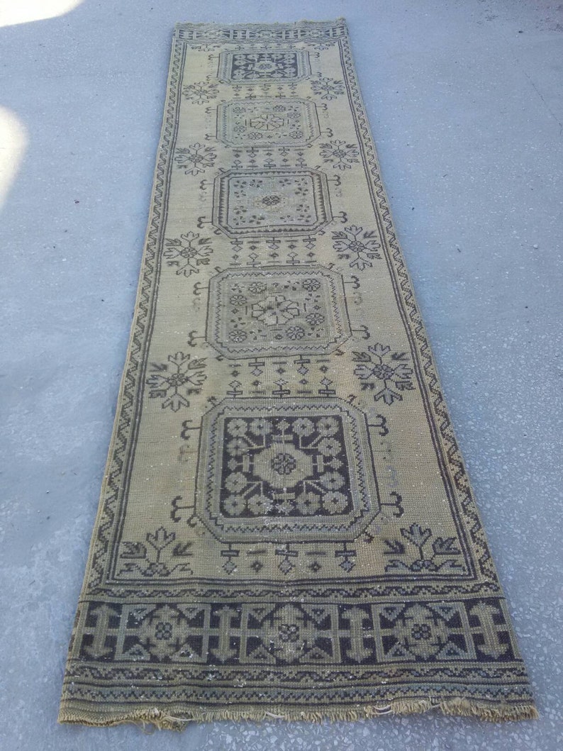 May include: A long, rectangular rug with a beige background and a black and white geometric pattern. The rug has a fringe border.