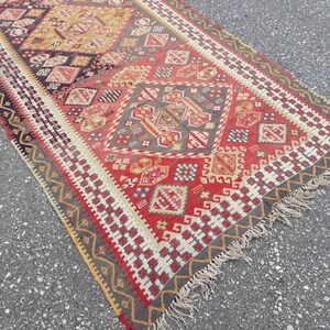 May include: A red, gray, and yellow patterned rug with a fringe border. The rug has a geometric design with repeating diamond shapes.