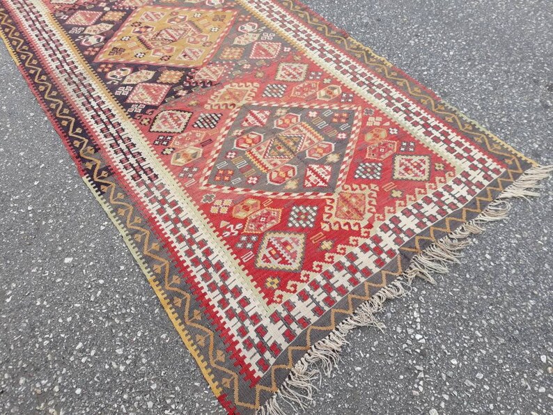 May include: A red, gray, and yellow patterned rug with a fringe border. The rug has a geometric design with repeating diamond shapes.