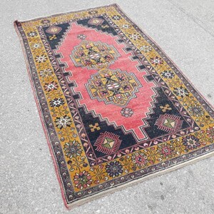 May include: A vintage rug with a traditional Persian design. The rug has a red center with black and yellow geometric patterns. The border is a yellow and gold floral design.