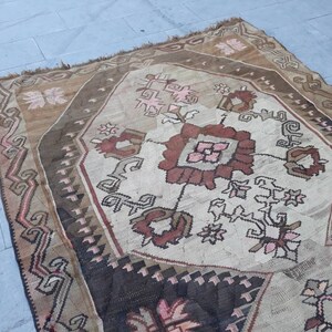 May include: A vintage Turkish rug with a geometric pattern in shades of brown, pink, and white. The rug has a worn and faded look, giving it a rustic and antique feel.