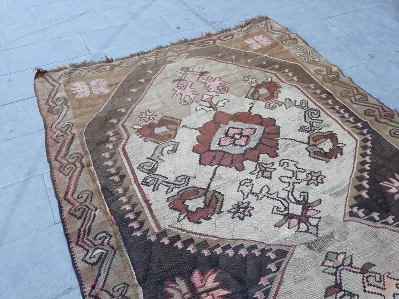 May include: A vintage Turkish rug with a geometric pattern in shades of brown, pink, and white. The rug has a worn and faded look, giving it a rustic and antique feel.