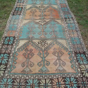 Puede incluir: Una alfombra turca vintage con un patr&oacute;n geom&eacute;trico en tonos azules, marrones y beige. La alfombra tiene un aspecto descolorido y desgastado y presenta un motivo de &aacute;rbol repetido.