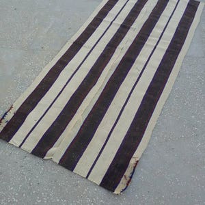 May include: A long, white and brown striped rug with a subtle purple hue. The rug is woven with a simple pattern and has a rustic, vintage look.