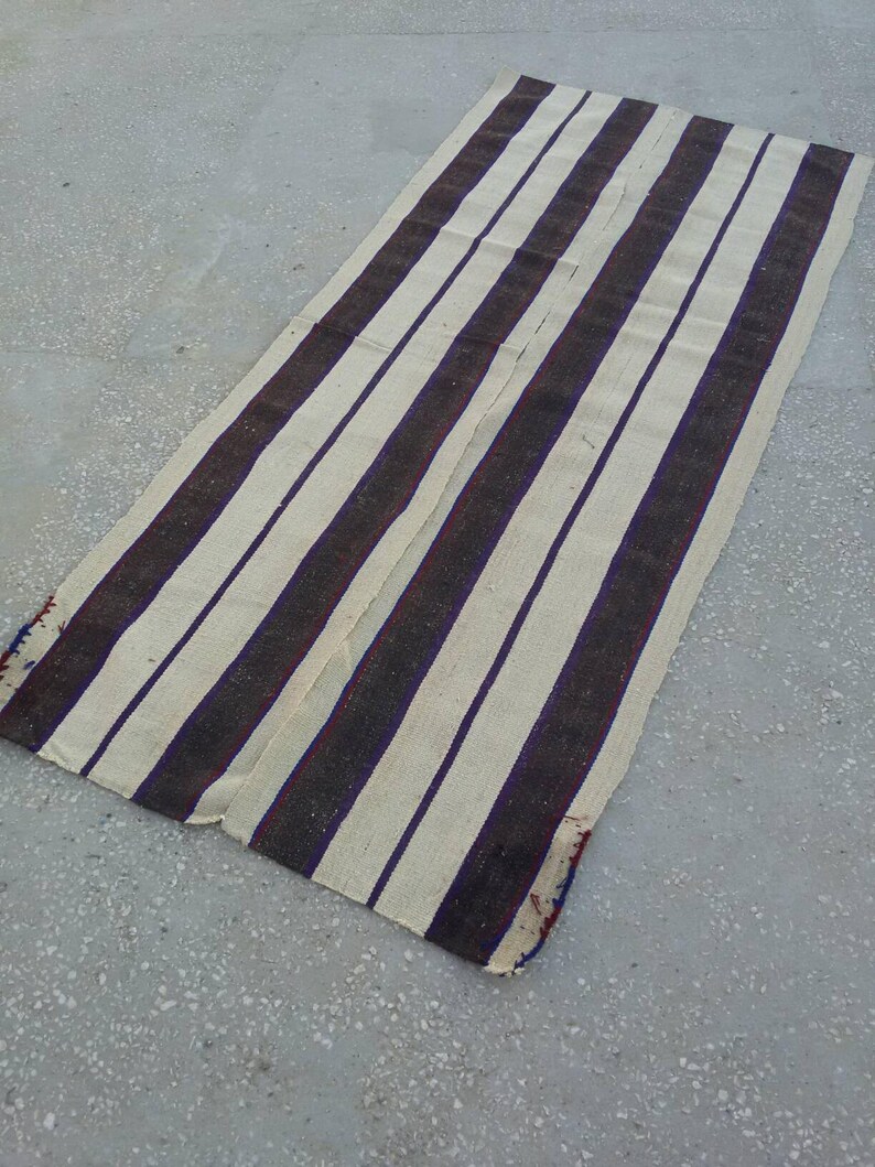 May include: A long, white and brown striped rug with a subtle purple hue. The rug is woven with a simple pattern and has a rustic, vintage look.