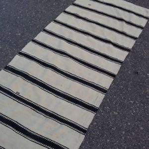 Pu&ograve; includere: Un tappeto a strisce bianche e nere con un design intrecciato. Il tappeto &egrave; fatto di fibra naturale e ha un aspetto rustico.