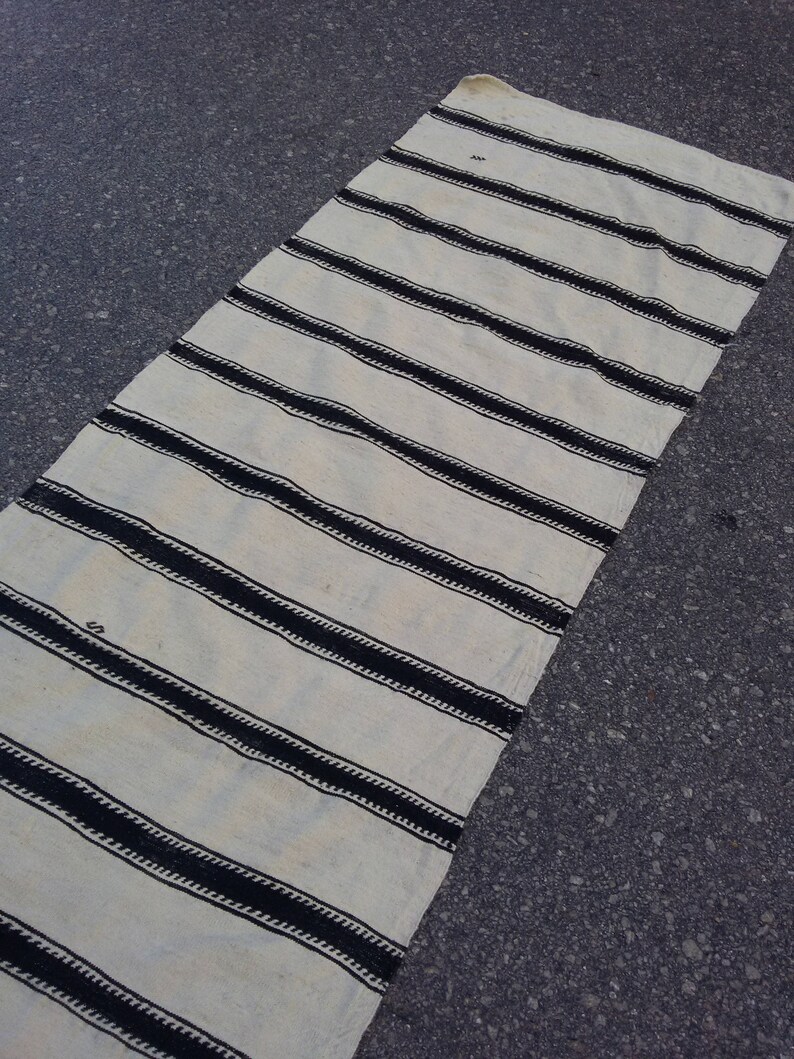 Pu&ograve; includere: Un tappeto a strisce bianche e nere con un design intrecciato. Il tappeto &egrave; fatto di fibra naturale e ha un aspetto rustico.