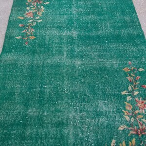 Pode incluir: Um tapete verde vintage com um padr&atilde;o floral desbotado em tons de rosa, amarelo e marrom. O tapete tem um aspecto desgastado e &eacute; feito de um material tecido.