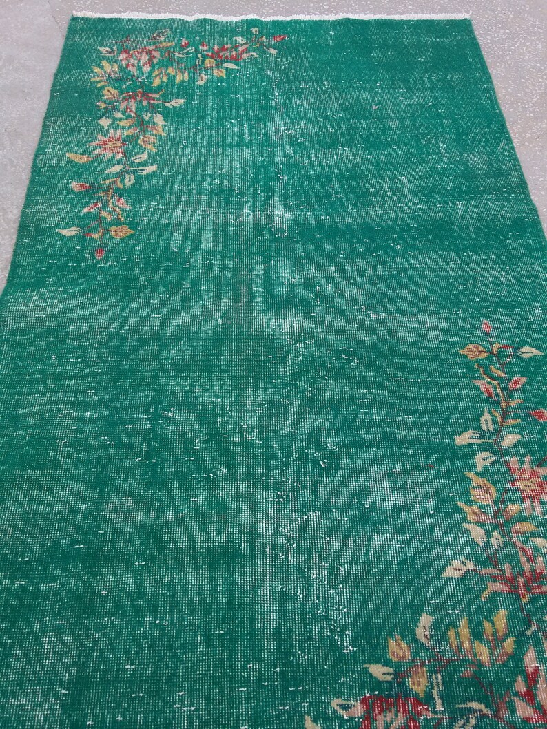 Pode incluir: Um tapete verde vintage com um padr&atilde;o floral desbotado em tons de rosa, amarelo e marrom. O tapete tem um aspecto desgastado e &eacute; feito de um material tecido.