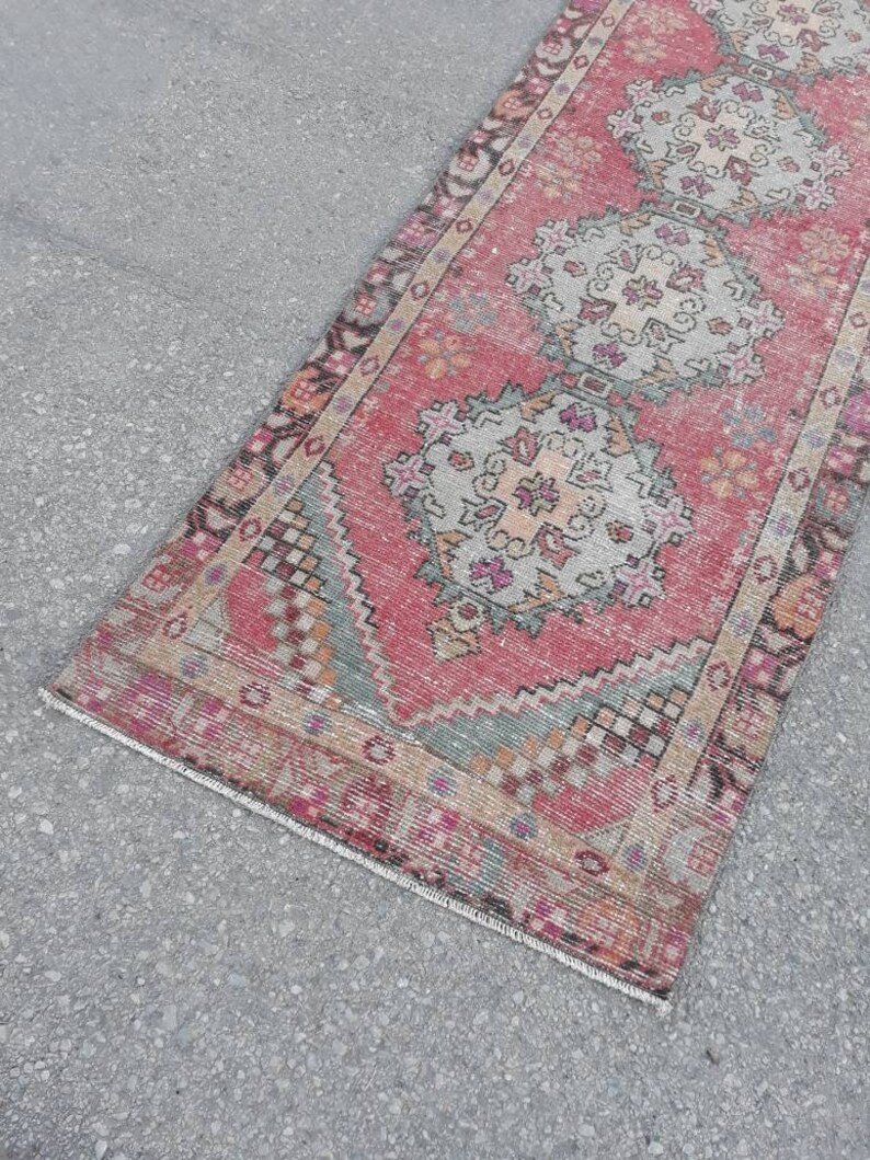 May include: A vintage pink and cream runner rug with a traditional floral pattern. The rug has a faded, distressed look and is perfect for adding a touch of bohemian style to your home.