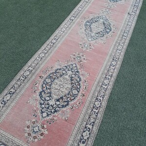 May include: A pink runner rug with a traditional Persian design featuring intricate floral patterns and a border of paisley motifs. The rug has a faded, vintage look.