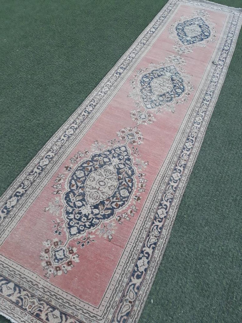 May include: A pink runner rug with a traditional Persian design featuring intricate floral patterns and a border of paisley motifs. The rug has a faded, vintage look.