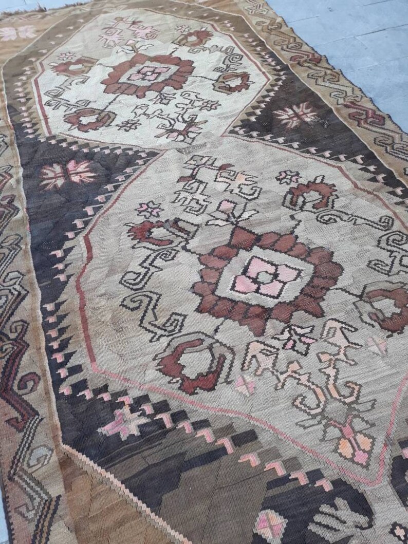 May include: A vintage rug with a geometric pattern in shades of brown, pink, and white. The rug has a worn and faded look, giving it a rustic and antique feel.