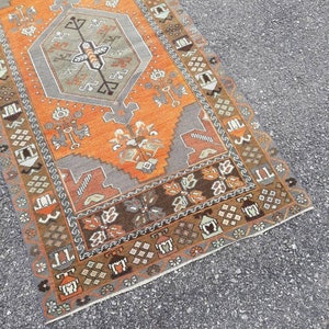 May include: A vintage Turkish runner rug with a geometric pattern in shades of orange, brown, and gray. The rug has a fringed edge and is made of wool.