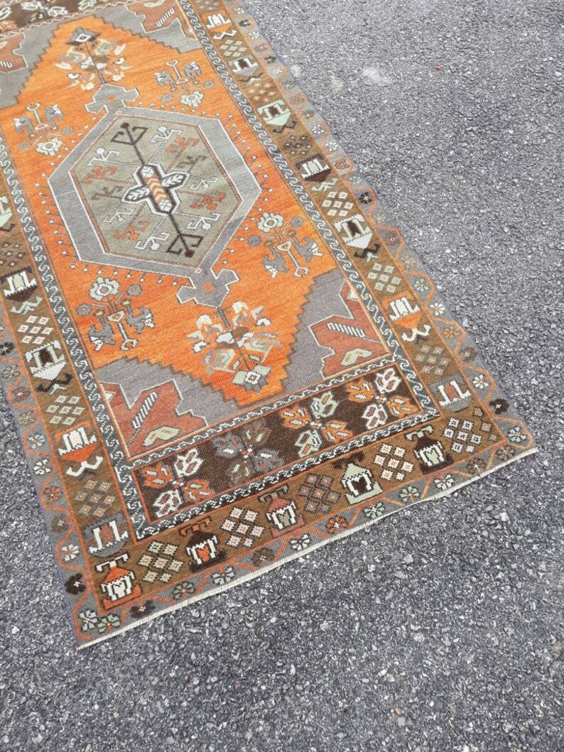 May include: A vintage Turkish runner rug with a geometric pattern in shades of orange, brown, and gray. The rug has a fringed edge and is made of wool.