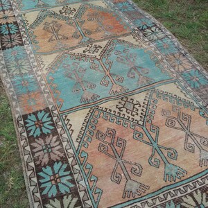 Puede incluir: Una alfombra turca vintage de corredor con un esquema de color turquesa, marr&oacute;n y crema. La alfombra presenta un patr&oacute;n geom&eacute;trico con motivos florales estilizados.