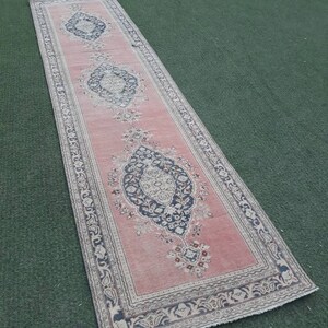 May include: A long, narrow pink rug with a floral pattern and a white border. The rug has a traditional design with intricate details.