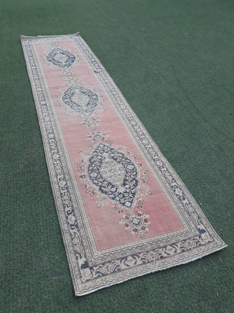 May include: A long, narrow pink rug with a floral pattern and a white border. The rug has a traditional design with intricate details.