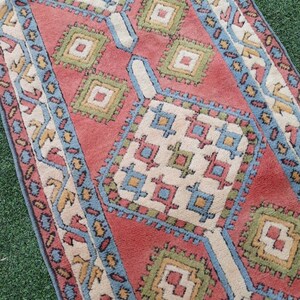 May include: A vintage rug with a geometric pattern in shades of red, blue, green, and white. The rug has a traditional design with repeating squares and diamonds.