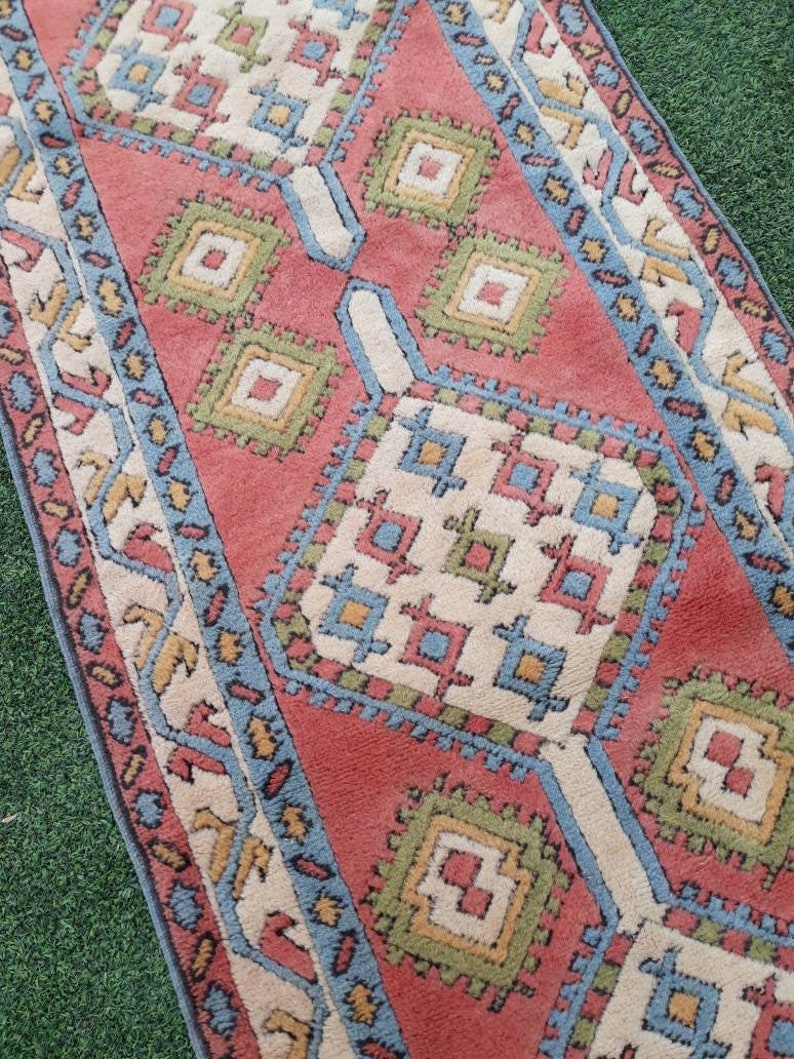 May include: A vintage rug with a geometric pattern in shades of red, blue, green, and white. The rug has a traditional design with repeating squares and diamonds.