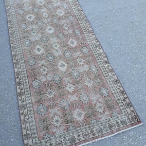K&ouml;nnte beinhalten: Ein Vintage-L&auml;ufer mit einem floralen Muster in Rosa-, Beige- und Gr&uuml;nt&ouml;nen. Der Teppich hat einen verblassten, abgenutzten Look und einen Fransenrand.