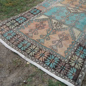 Puede incluir: Una alfombra turca vintage con un patr&oacute;n geom&eacute;trico en tonos marrones, azules y beige. La alfombra tiene un borde de flecos blancos.