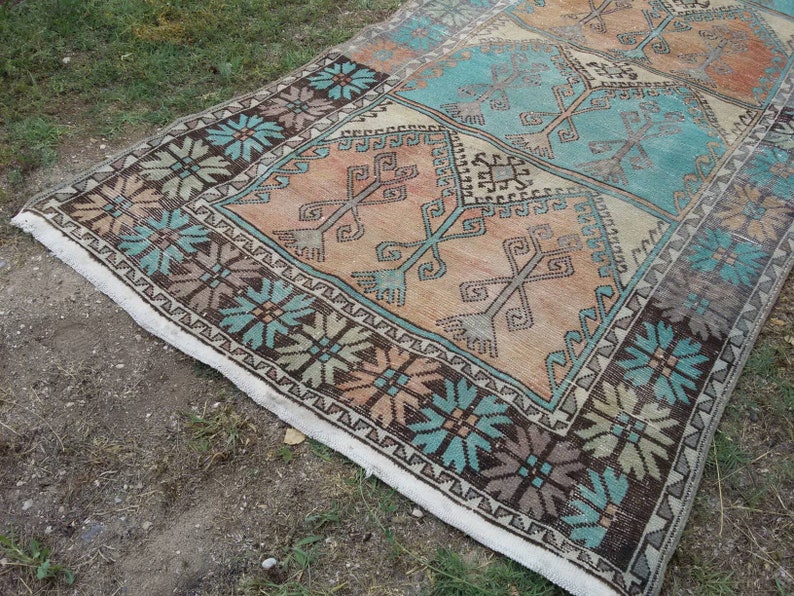 Puede incluir: Una alfombra turca vintage con un patr&oacute;n geom&eacute;trico en tonos marrones, azules y beige. La alfombra tiene un borde de flecos blancos.