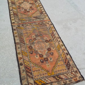 May include: A vintage runner rug with a geometric pattern in shades of brown, orange, and cream. The rug has a fringed edge and is made of wool.