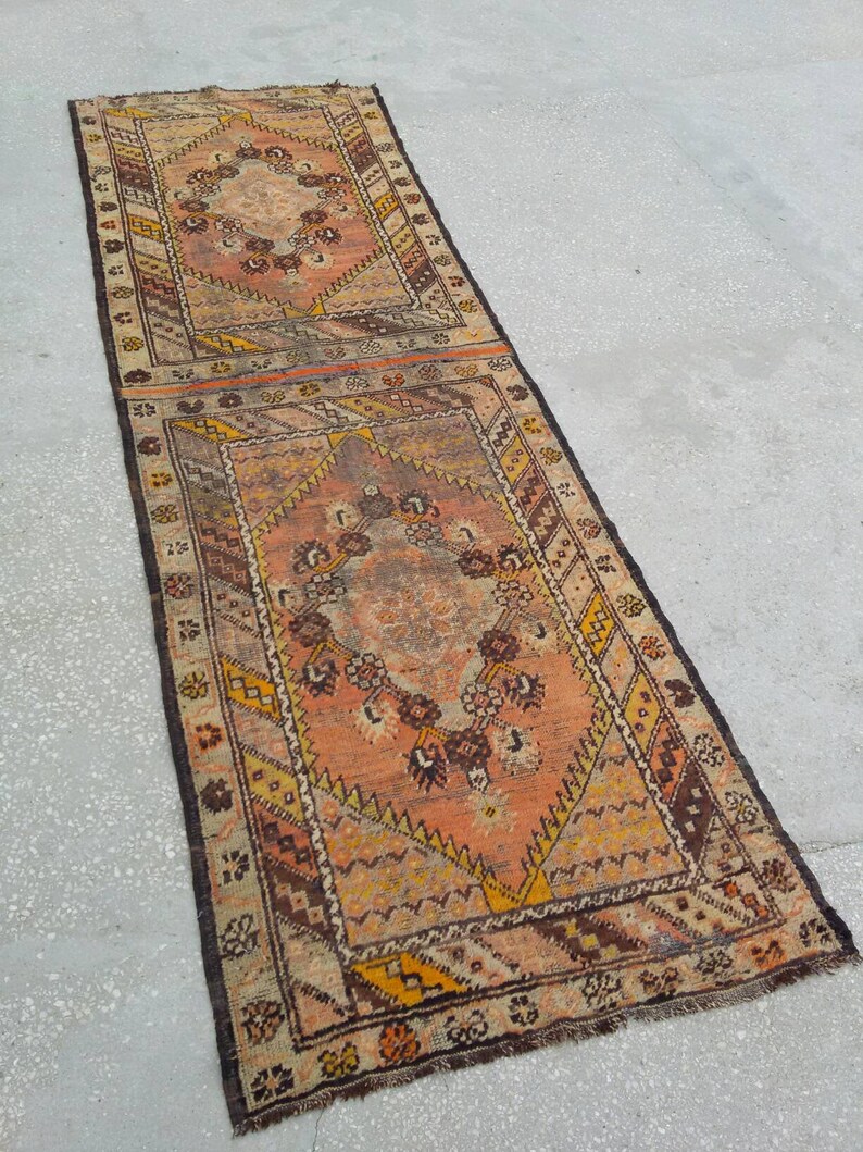 May include: A vintage runner rug with a geometric pattern in shades of brown, orange, and cream. The rug has a fringed edge and is made of wool.