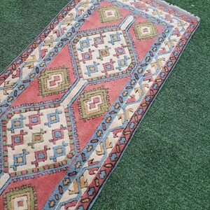 May include: A red, blue, and green patterned rug with a geometric design. The rug has a fringed edge and is laid out on a green surface.