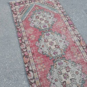 May include: A vintage Turkish runner rug with a red background and intricate floral patterns in shades of pink, blue, and white. The rug has a faded, distressed look, giving it a unique and charming character.