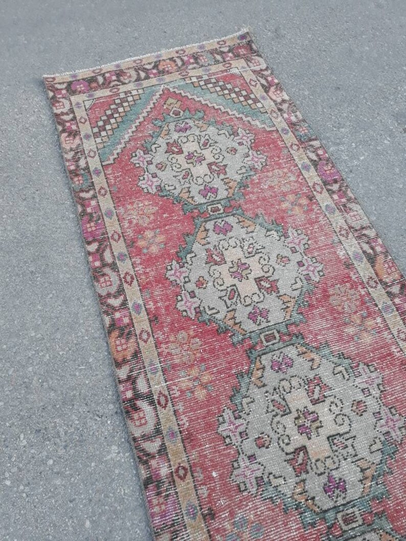 May include: A vintage Turkish runner rug with a red background and intricate floral patterns in shades of pink, blue, and white. The rug has a faded, distressed look, giving it a unique and charming character.