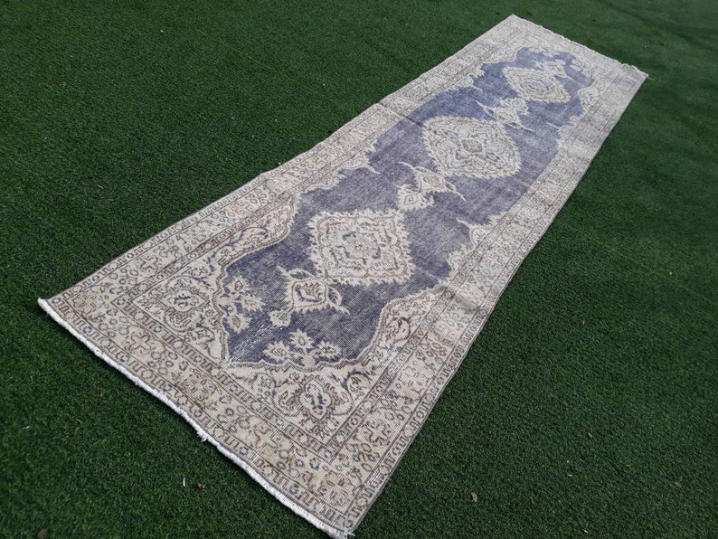 May include: A long, rectangular rug with a cream and blue patterned design. The rug has a faded, vintage look and is perfect for adding a touch of bohemian style to any room.