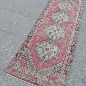 May include: A vintage pink and cream runner rug with a traditional floral pattern. The rug has a faded, distressed look and is approximately 2 feet wide and 6 feet long.